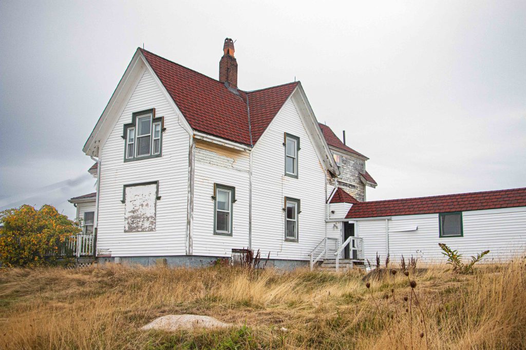 The historic Lightkeeper’s House at Eastern Point in Massachusetts, set against an overcast sky and surrounded by rugged vegetation