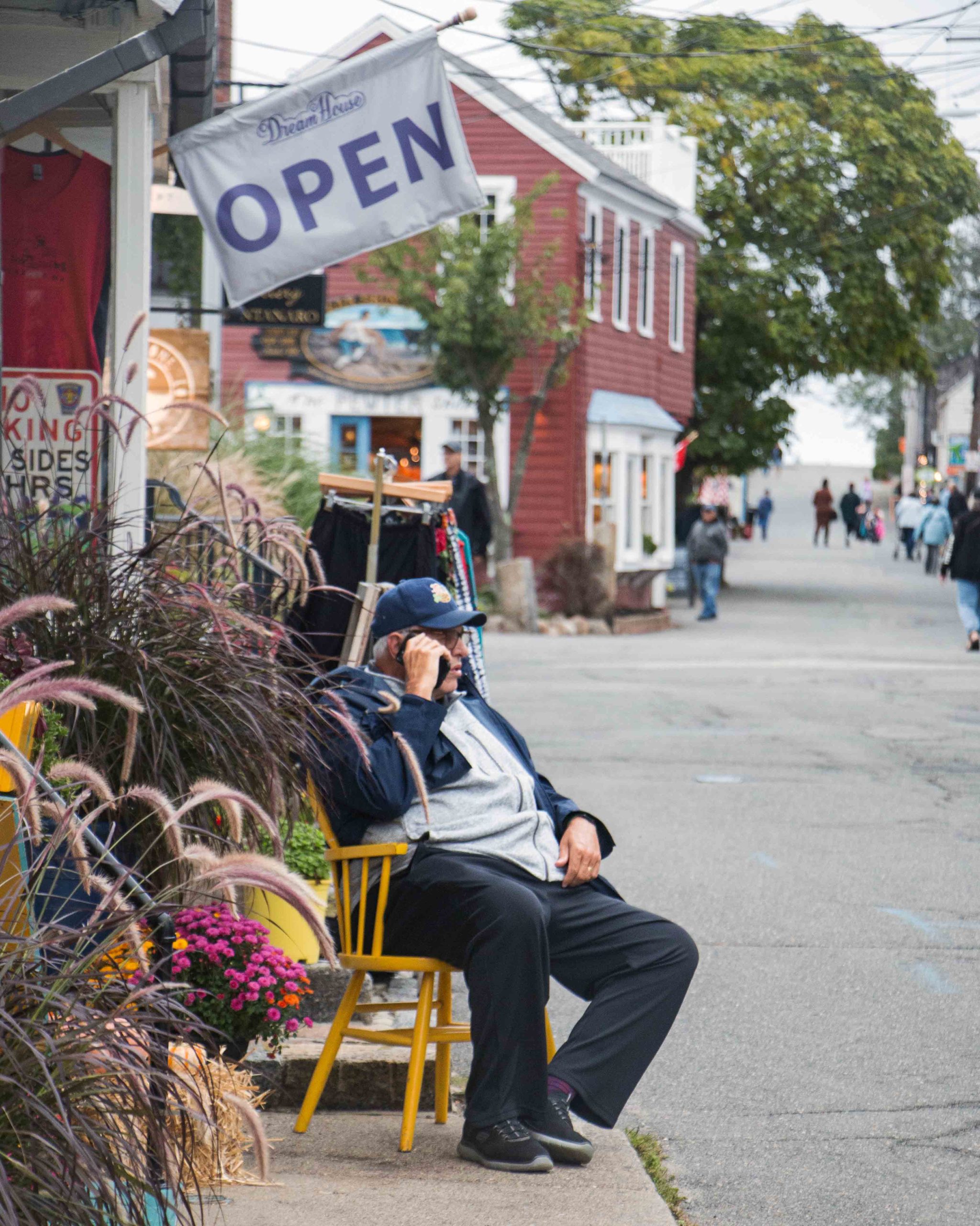 A quaint open sign on display in front of a local shop in Rockport, Massachusetts, with a person seated outside