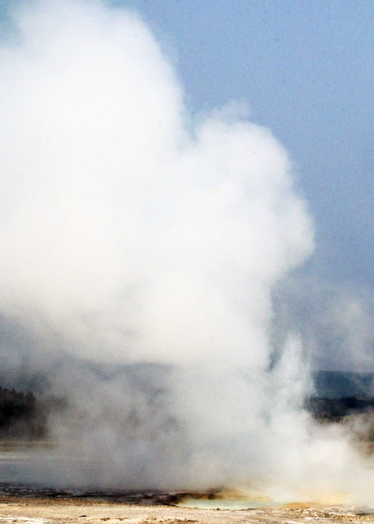 Steam and water erupting from Old Faithful Geyser under a clear blue sky.